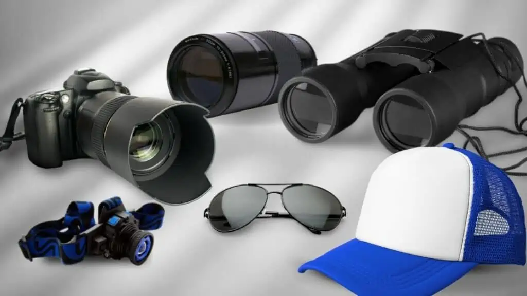 A dslr camera, separate lens, binocular, head light, sunglasses and a baseball cap