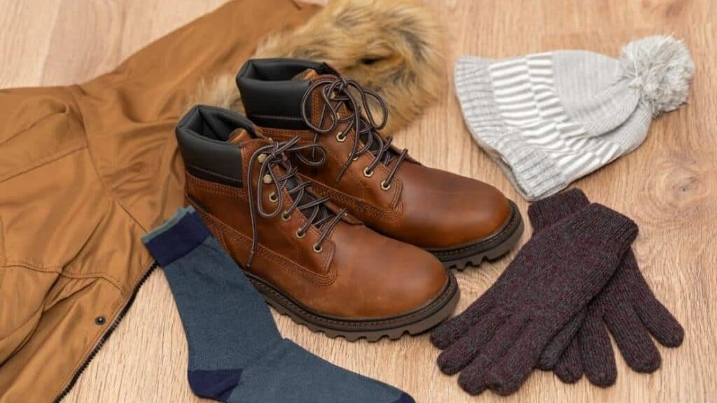 A brown jacket, a pair of boots and socks, gloves and beanie hat for your Alaska packing list